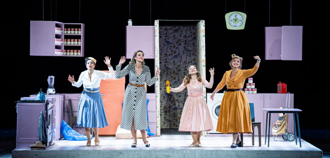 Scene from Falstaff where four women stand on stage in a set that replicates a house.