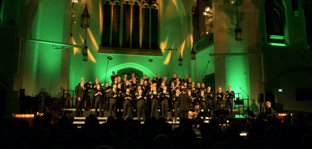 Chor Leoni conducted by Erick Lichte standing in a church while surrounded by green and gold lighting