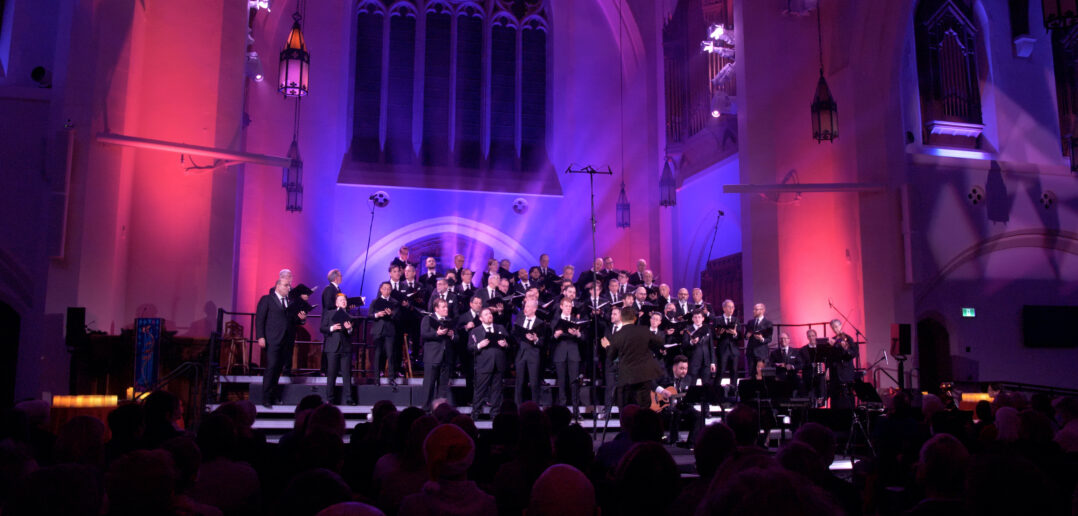 Chor Leoni conducted by Erick Lichte while in a church surrounded by purple and pink lighting